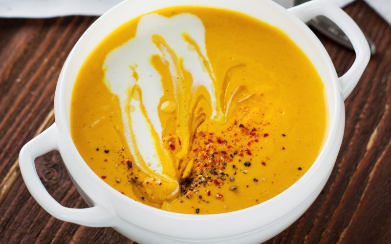 Pumpkin soup with turmeric, lime and coconut in white bowl on rustic wooden table