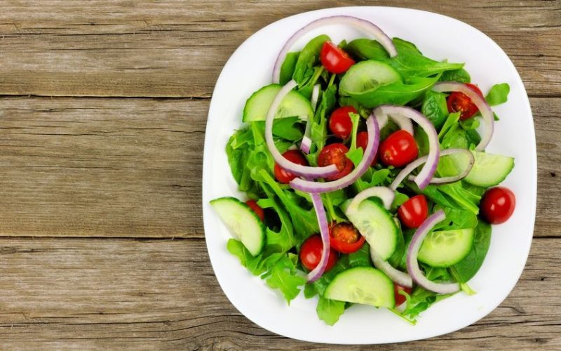 38490233 - salad with greens cherry tomatoes red onions and cucumber on white plate with wood background overhead view